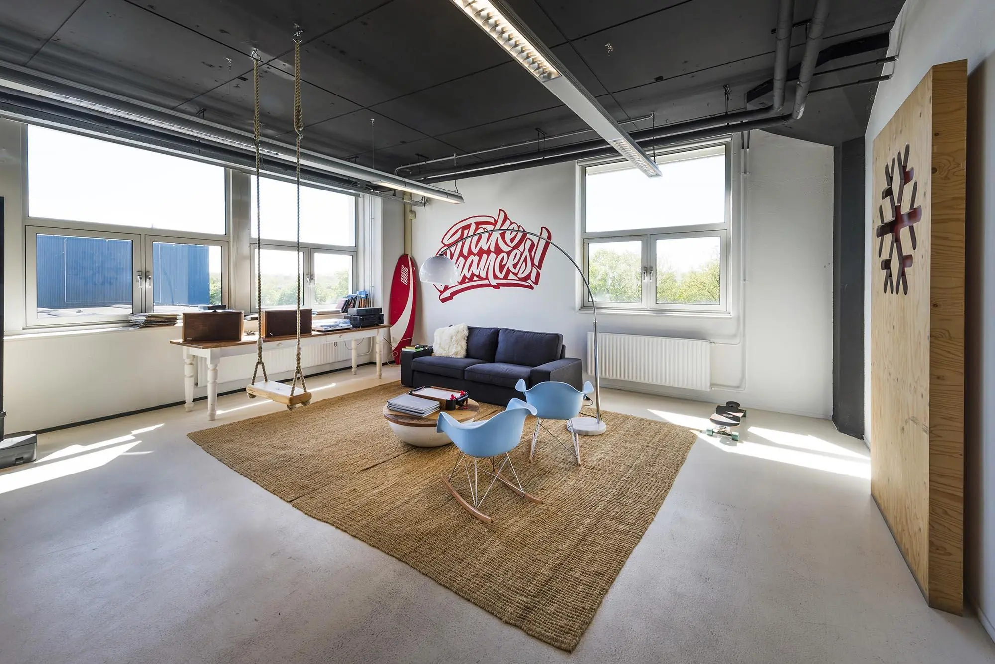 Modern ingerichte kantoorruimte aan de Anthony Fokkerweg met een zithoek, schommel en muurschildering met de tekst "Take Chances".